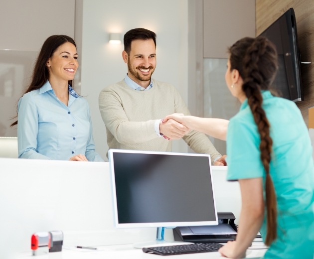 Oral surgery team member greeting two patients at reception desk