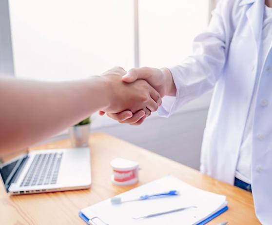 Two people shaking hands across desk in dental office