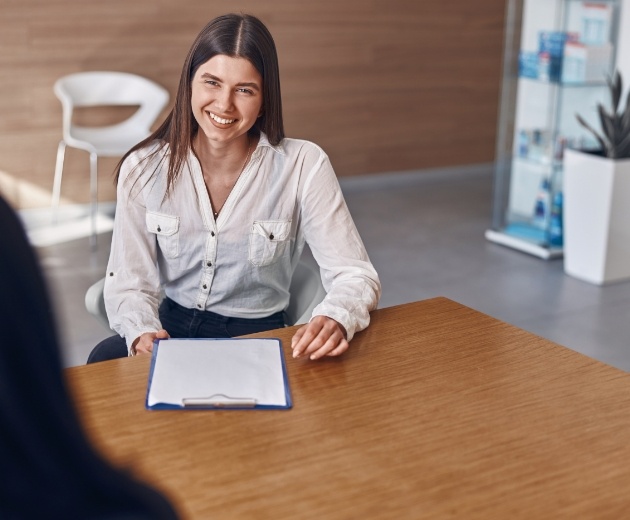 Smiling woman sitting at desk with clipboard for dental and medical insurance in Reston